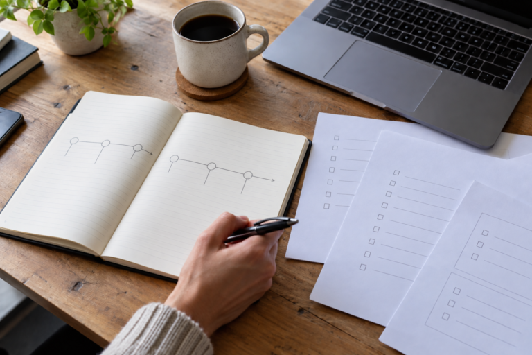 Open notebook with a project timeline and checklists beside a laptop on a wooden desk.